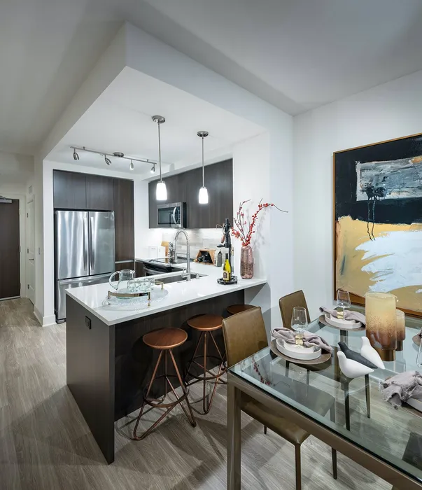 Open-concept kitchen and dining area with a 4-person dining table, dark wood cabinets, stainless appliances, and a quartz-topped peninsula