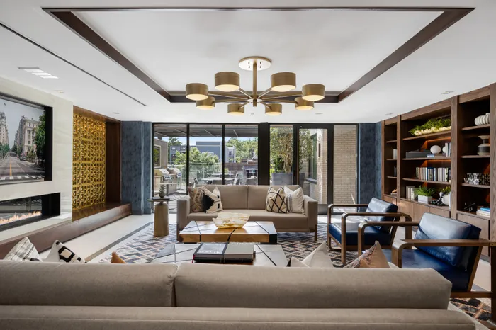 Resident Lounge with floor-to-ceiling windows, upholstered armchairs and sofas with coffee tables centered around a gas indoor fireplace.