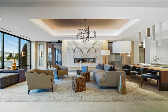 decorated lobby that has two accent chairs, a large sofia, communal table with chairs and a fireplace in the baclground