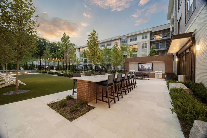 courtyard with two grills and two dining tables next to a green lawn space with lounge chairs