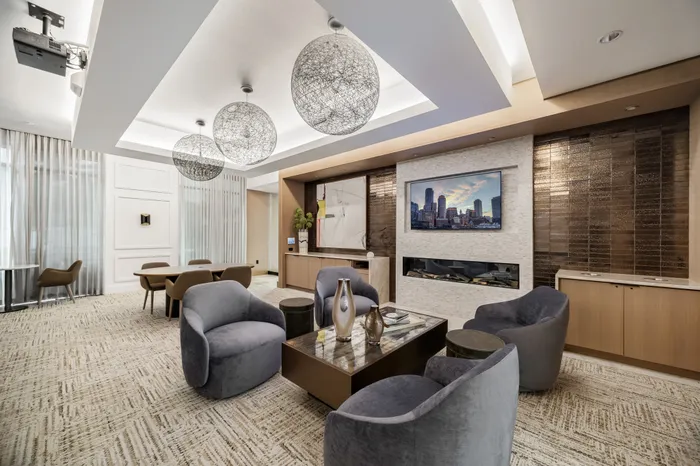 lounge area with two seating areas with 4 tables around a center table next to a wall with a fireplace and TV
