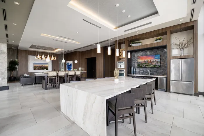 large clubroom with kitchen with waterfall granite counters and 8 counter chairs and stainless steel french door fridge and more seating areas in the background