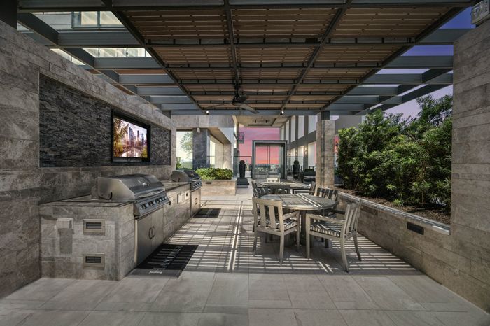 Elevated deck with two built-in grilling stations against a stone wall with a TV next to two round 4-person dining tables