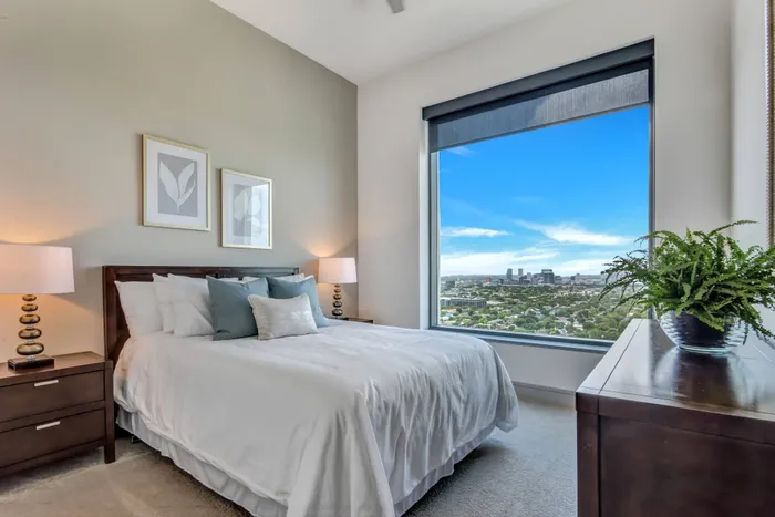 apartment bedroom with king size bed and two night stands and dresser, oversized picture window showing sweeping Houston views