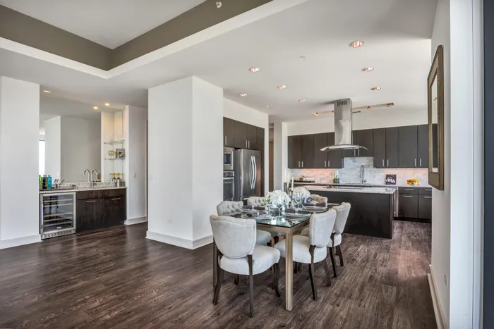 Kitchen and dining area with wet bar with wine fridge, 6-seater dining table, and a kitchen with floating vent hood and spacious kitchen island and brown tone cabinets