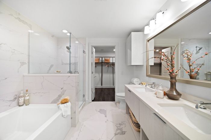 bathroom with white marble tiling and white wood cabinetry, featuring soaking tub, glass shower and double vanity