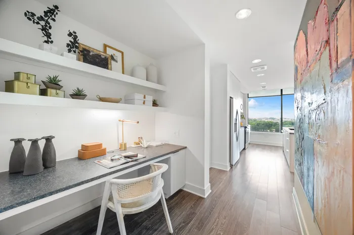 apartment entryway with built-in desk featuring open shelves and black granite counter tops, adjacent to kitchen with floor-to-ceiling windows