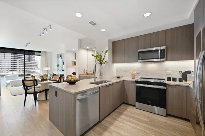 u-shaped kitchen in an apartment with brown-tone wood cabinetry, neutral stone counters, and stainless steel appliances