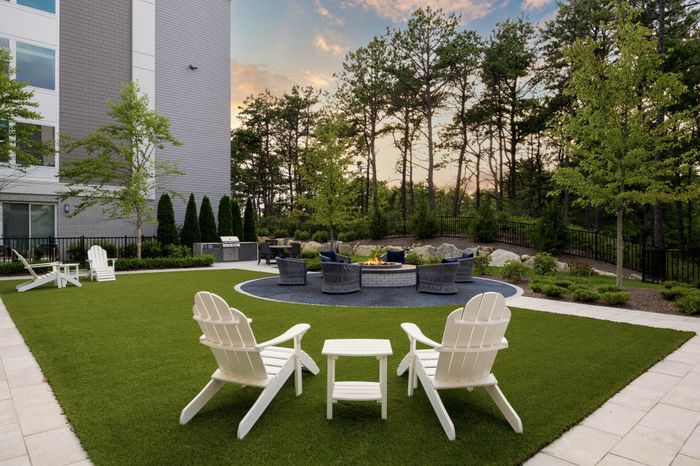 green lawn with two sets of adirondack chairs in the corners and a round fire pit in the middle with more chairs