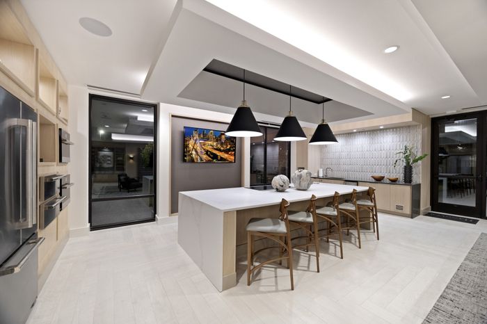 club room kitchen with large waterfall counter and chairs, glass top range, french door stainless steel fridge and TV