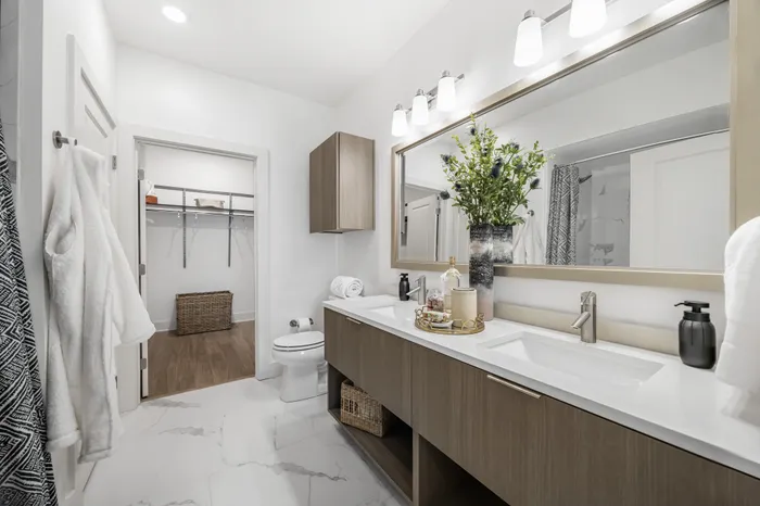 bathroom with white marble tile floors and double vanity with framed mirror, with closet attached