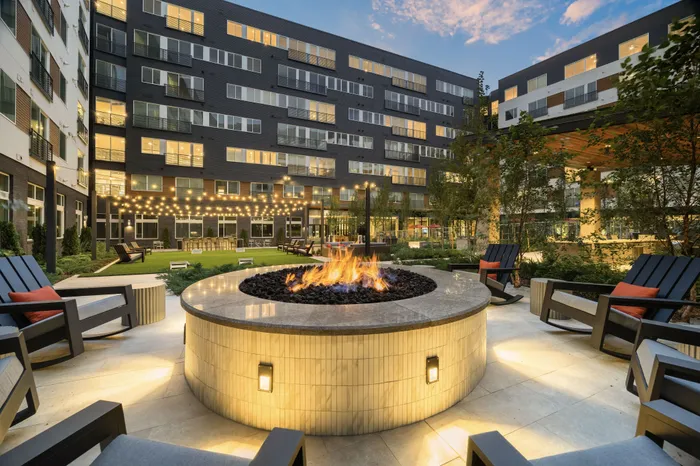 firepit in apartment courtyard surrounded with outdoor chairs, with string lights and lawn space behind