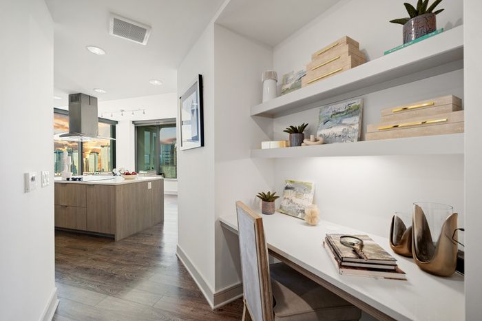 hallway with built in desk, a shair and two shelves above the desk with the kitchen in the background