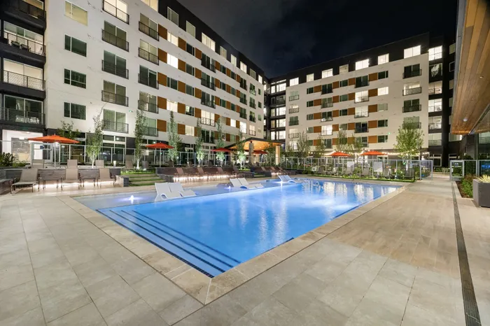 pool in courtyard of apartment building with in water chairs and two rows of sun-loungers next to the pool