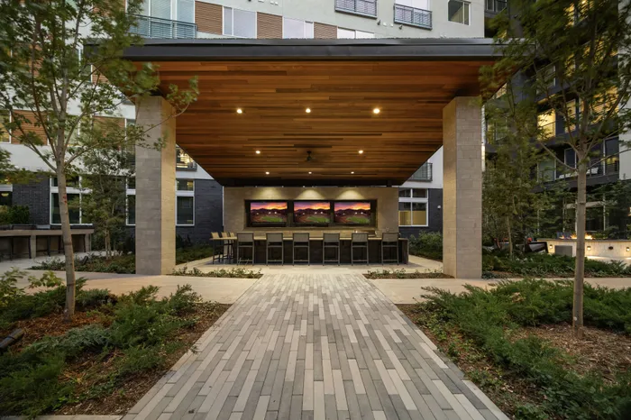 outdoor arbor with wood paneled ceiling, 3 tvs, and counter-height bar with 9 stools around it