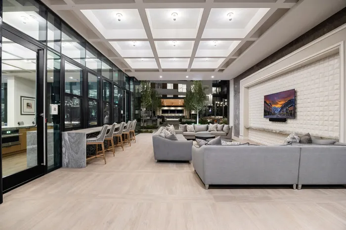open air covered lounge with sectional sofas, tvs, and counterstools facing a counter with windows that open to the inside