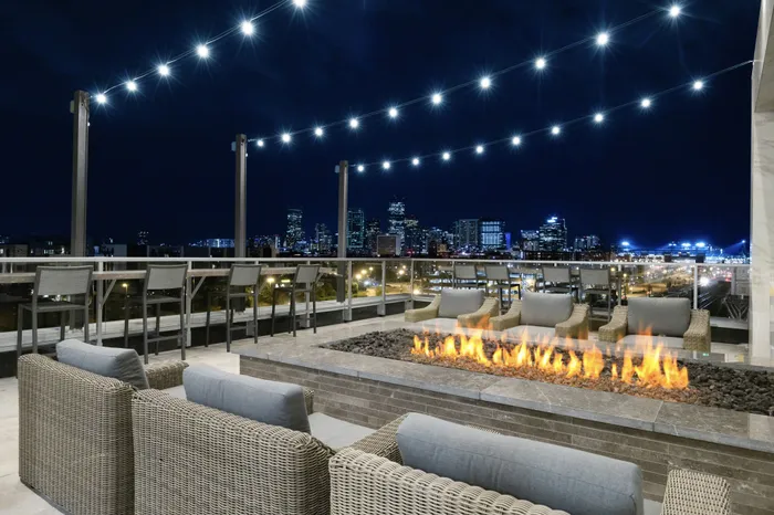 sky deck with string lights, low stone fireplace, lounge seating, and bar ledge with stools over looking downtown Denver at night