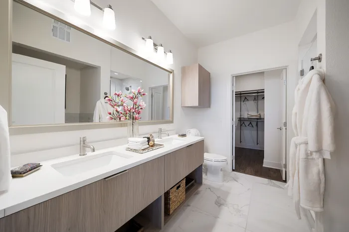 vanity of bathroom with two sinks, framed mirror, toilet and closet attached