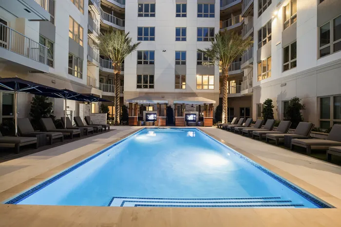pool of apartment community lit up at night with cushioned lounge chairs and cabanas
