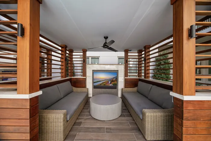 covered cabana with open wood-slate dividers, two couches, TV, and ceiling fan