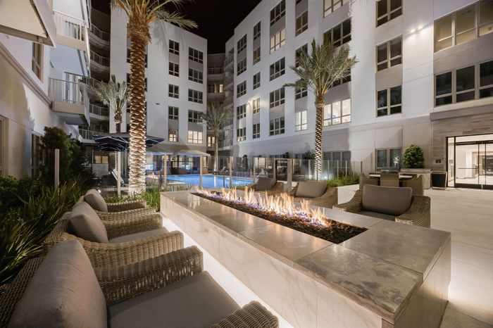 courtyard of 6-story apartment building with rectangular open fire pit surrounded by 6 cushioned chairs