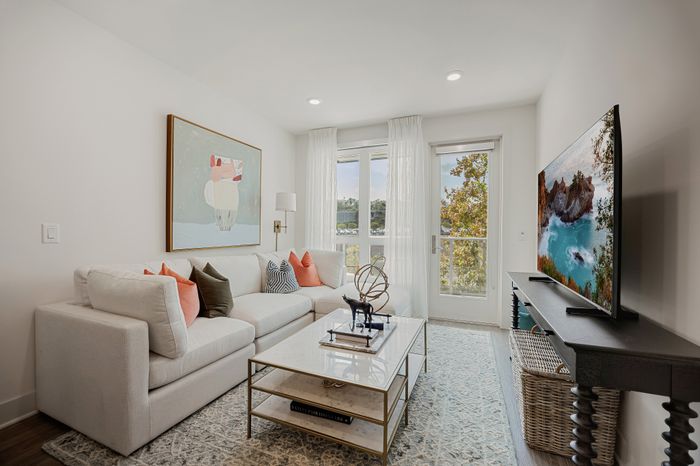 living room in apartment with sectional sofa and TV and large oversized windows and glass door leading to balcony