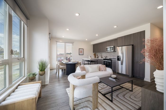 Living room and kitchen of corner unit apartment with brown wood floors, wood style cabinets and free standing island.