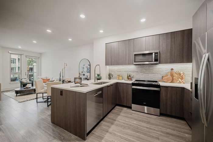 apartment with u-shaped kitchen with brown cabinets, white counters and stainless steel appliances and living space beyond