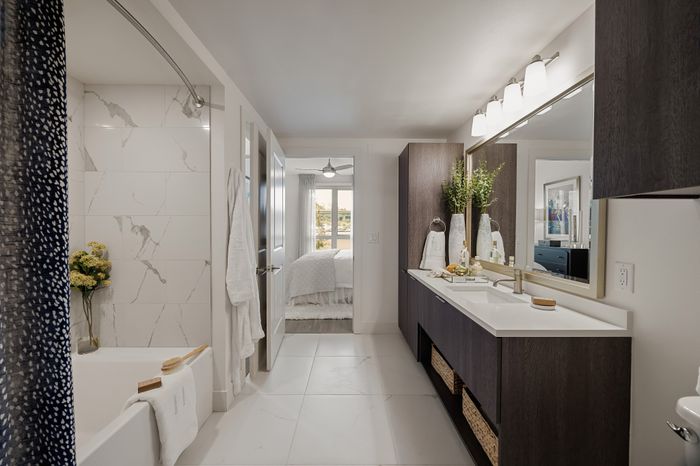 en suite bathroom with single vanity with storage below, framed mirror, and soaking tub with tile surround