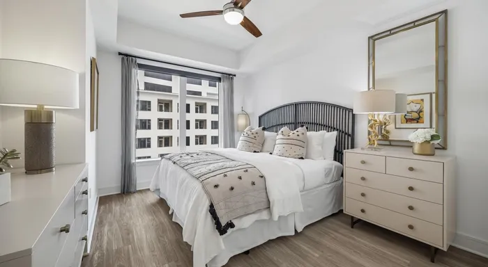 Elegant bedroom with stylish decor, featuring a comfortable bed, chic dresser, and large window with city view.