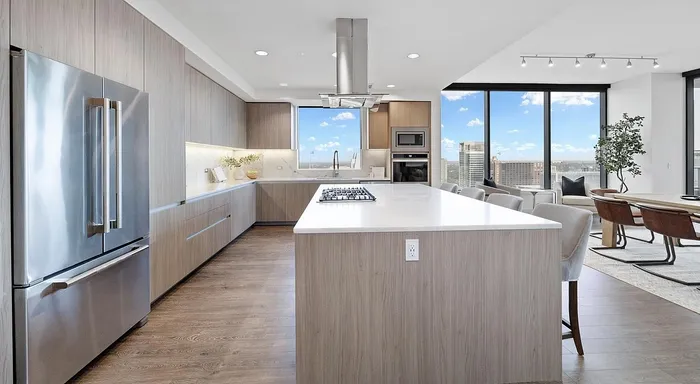 Modern open-concept kitchen and living area with sleek cabinetry, expansive island, and stunning city views through floor-to-ceiling windows.