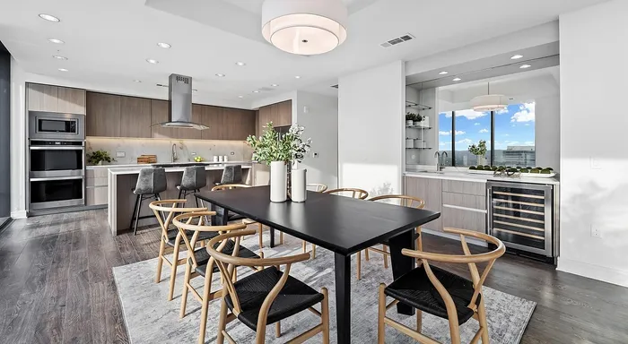 Modern open-concept kitchen and dining area featuring sleek wooden cabinetry, a stylish black dining table with elegant chairs, and large windows offering panoramic city views.