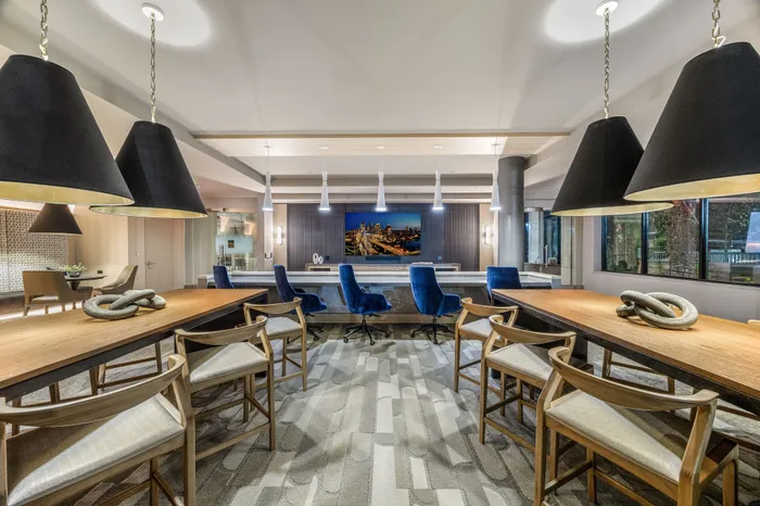 Elegant communal lounge with modern pendant lighting, plush blue chairs, and large windows offering a scenic view, ideal for social gatherings and meetings.