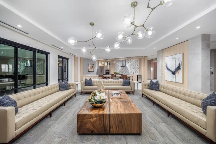 Elegant living room with modern decor, featuring plush beige sofas, a chic wooden coffee table, stylish lighting fixtures, and a spacious open kitchen.