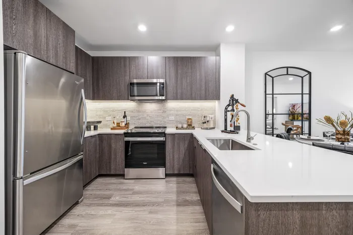 Modern kitchen with sleek stainless steel appliances, dark wood cabinetry, and a spacious white island counter.