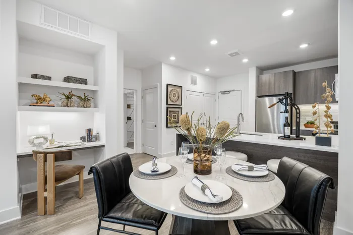 Modern apartment interior showcasing an elegant dining area with a chic round table, stylish black chairs, and decorative centerpiece, complemented by a sleek open kitchen with contemporary cabinetry and accent lighting.