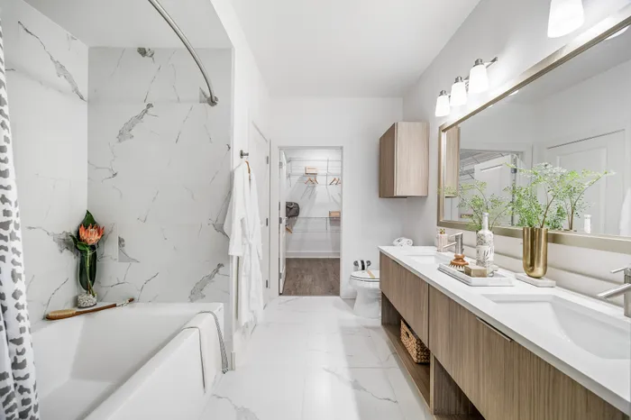 Luxurious modern bathroom featuring marble tile, dual sinks, elegant decor, and a spacious walk-in closet.