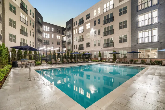 Luxurious apartment complex with a sparkling outdoor pool, modern design, and elegant lounging areas under serene evening lighting.