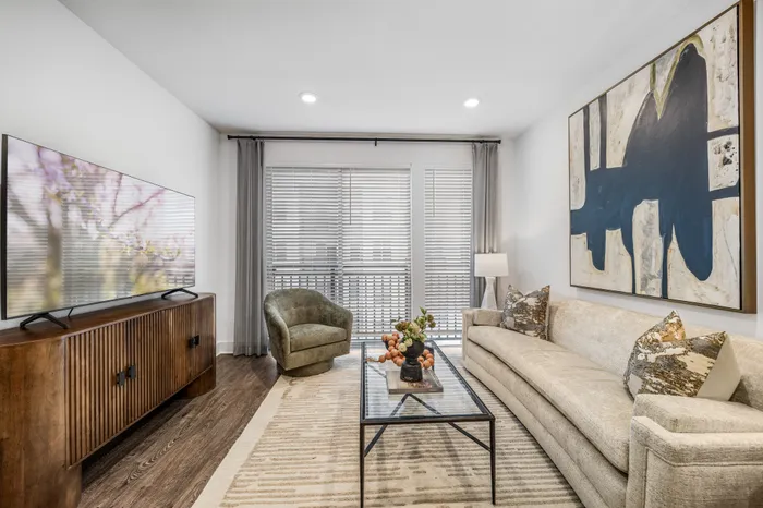 Modern living room with elegant decor, featuring a plush beige sofa, large abstract art, and floor-to-ceiling windows for natural light.