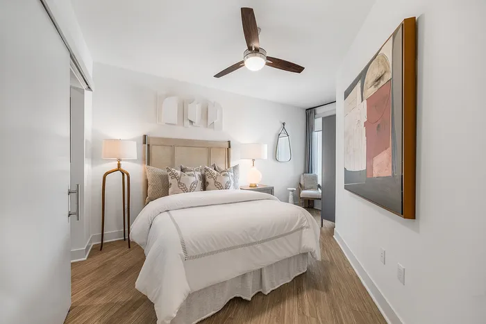Elegantly designed bright bedroom featuring a cozy bed, modern artwork, and stylish lighting, with hardwood flooring.