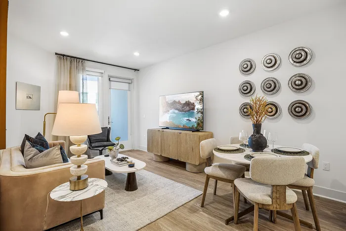 Modern living and dining area featuring elegant decor, a cozy beige sofa, stylish lamp, tasteful wall art, and a large flat-screen TV.