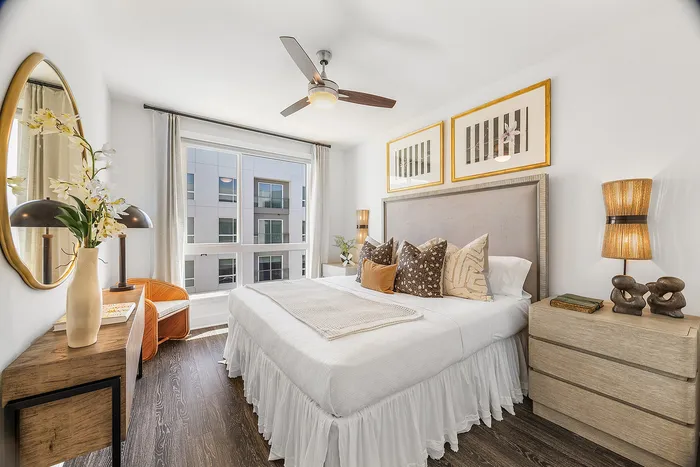 Bright and elegant bedroom with chic decor, featuring a cozy bed, modern ceiling fan, large window, and stylish accents.
