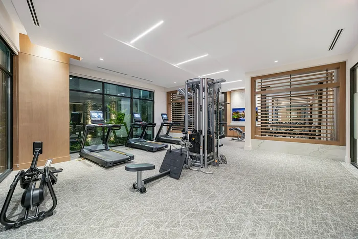 Luxurious fitness center featuring state-of-the-art cardio machines, strength training equipment, and expansive windows with garden views.