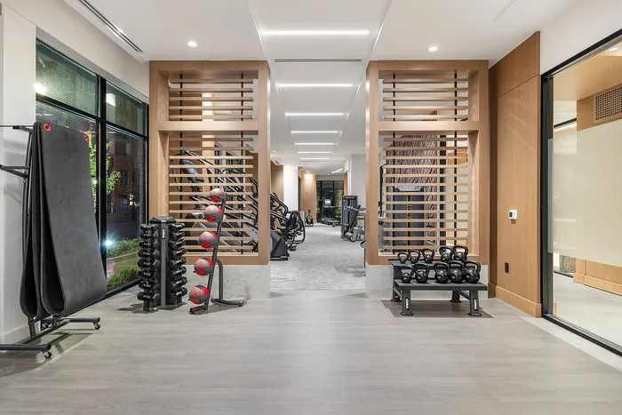 Contemporary gym space with sleek wooden accents featuring a variety of modern exercise equipment and a serene view through large windows.