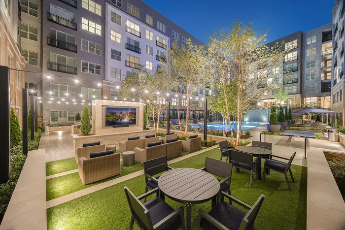Luxurious apartment courtyard featuring elegant outdoor seating, sparkling pool, ambient string lights, and lush greenery, perfect for relaxation and entertainment.