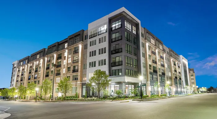 Elegant multi-story apartment building with modern architecture, illuminated against a twilight sky, surrounded by lush landscaping.