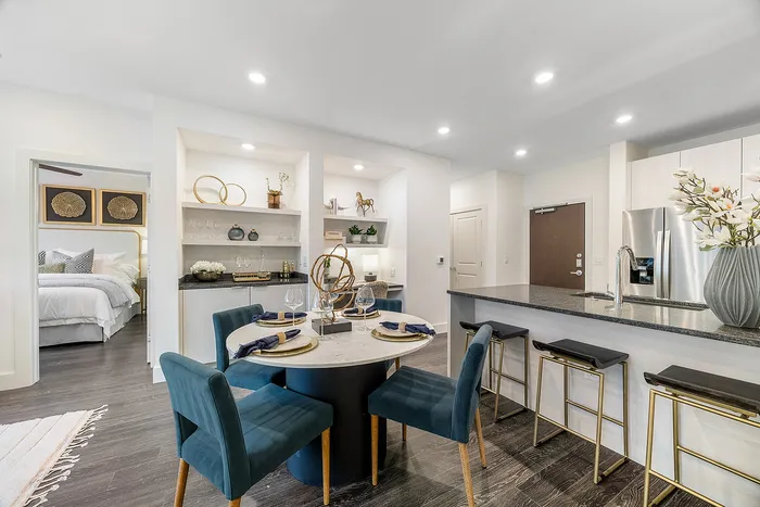 Modern open-concept kitchen and dining area with stylish decor, featuring a cozy table setting for four and sleek bar stools under granite countertop.