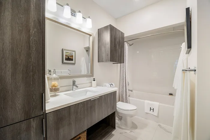 Elegant bathroom featuring modern fixtures, sleek wooden cabinetry, and a stylish shower-tub combo, exuding a spa-like ambiance.