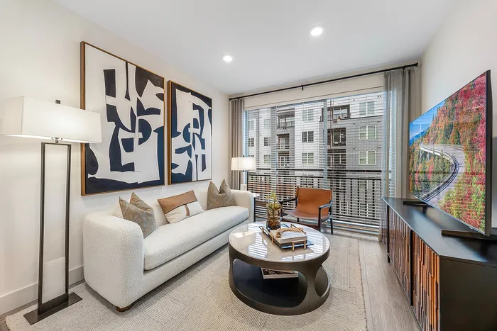 Contemporary living room with a cozy white sofa, abstract art, and large windows offering a view of urban architecture.