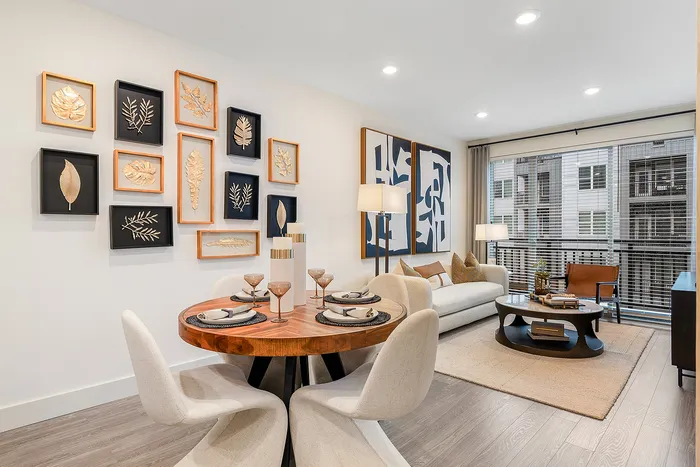 Modern living and dining area with elegant wall art, featuring a cozy round table set for four, plush cream chairs, and an inviting sofa with stylish decor in a bright, well-lit space.